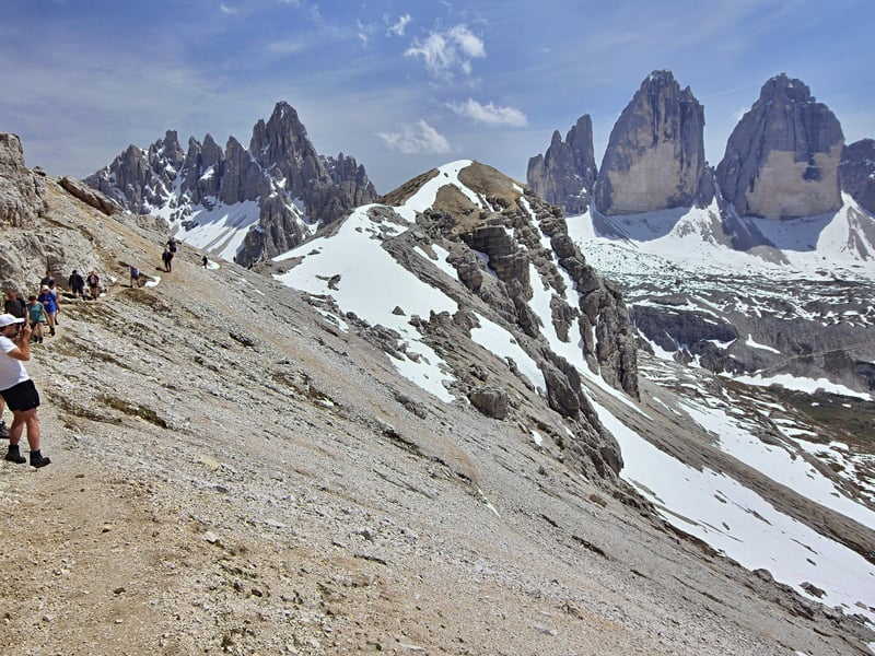 Turisté na stezce s výhledem na Tre Cime di Lavaredo v Dolomitech
